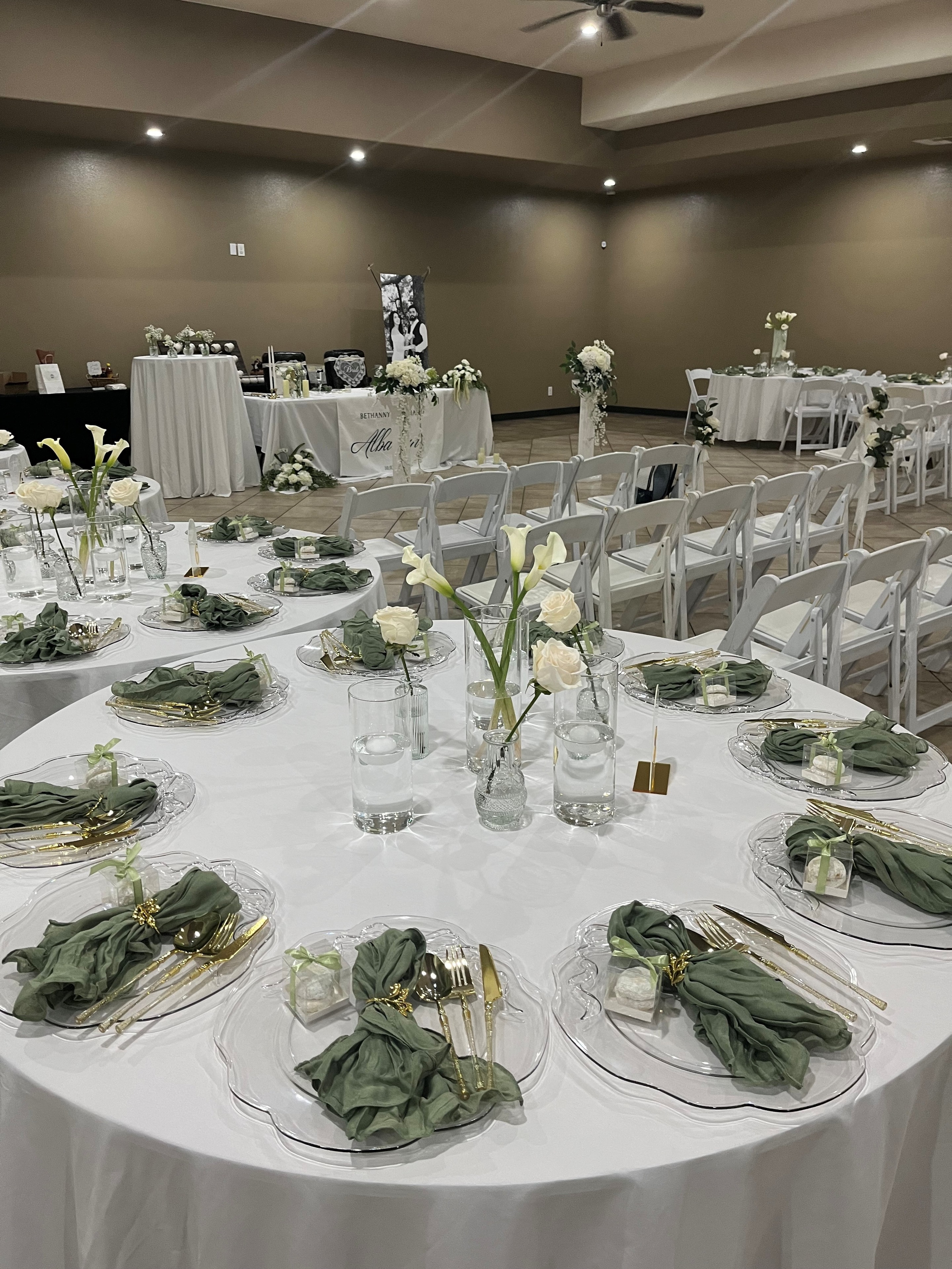 Wedding reception setup with white linens, green napkins, floral centerpieces, and gold flatware