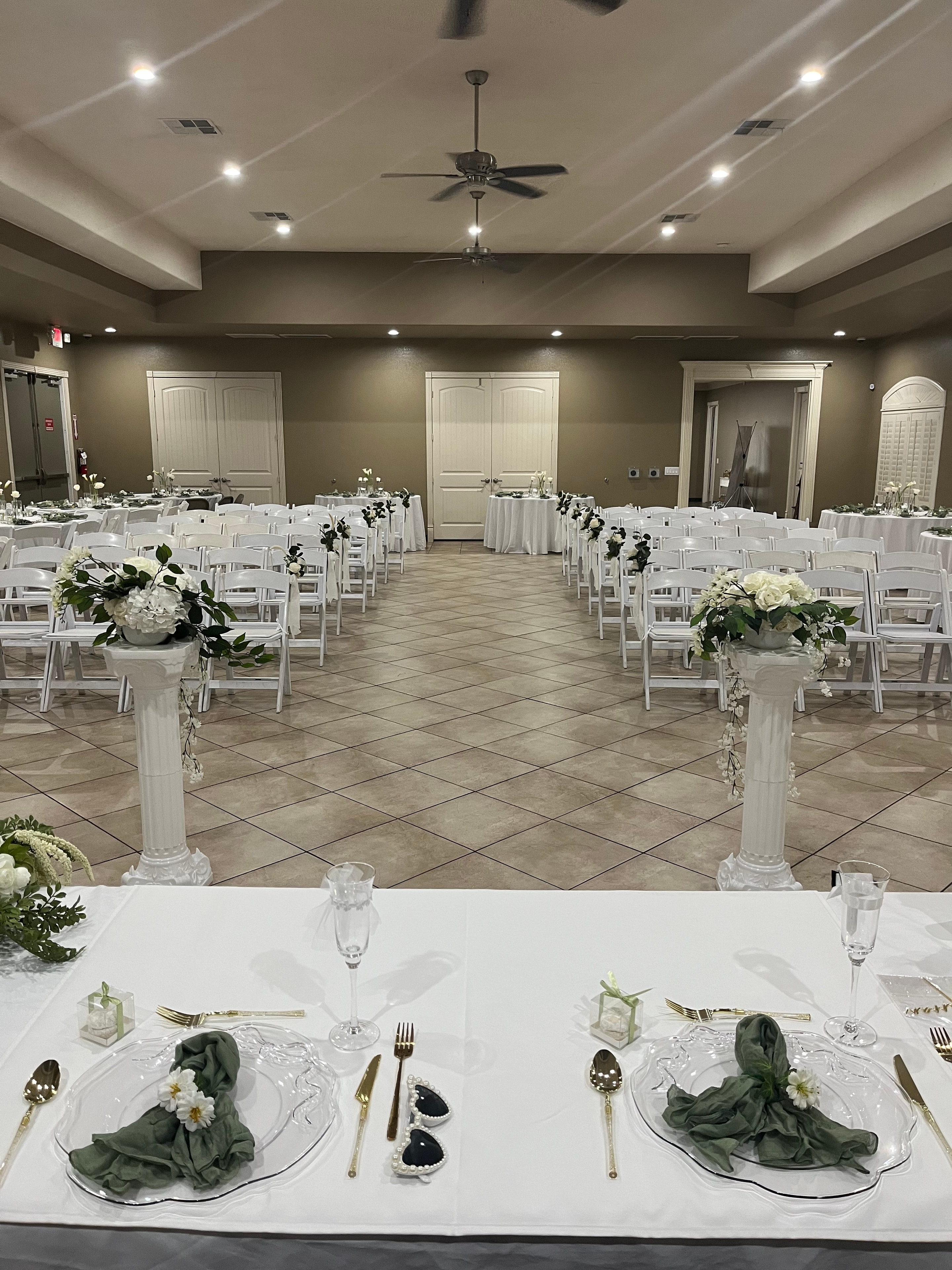 Elegant wedding reception table setting with white chairs, floral centerpieces, and gold flatware